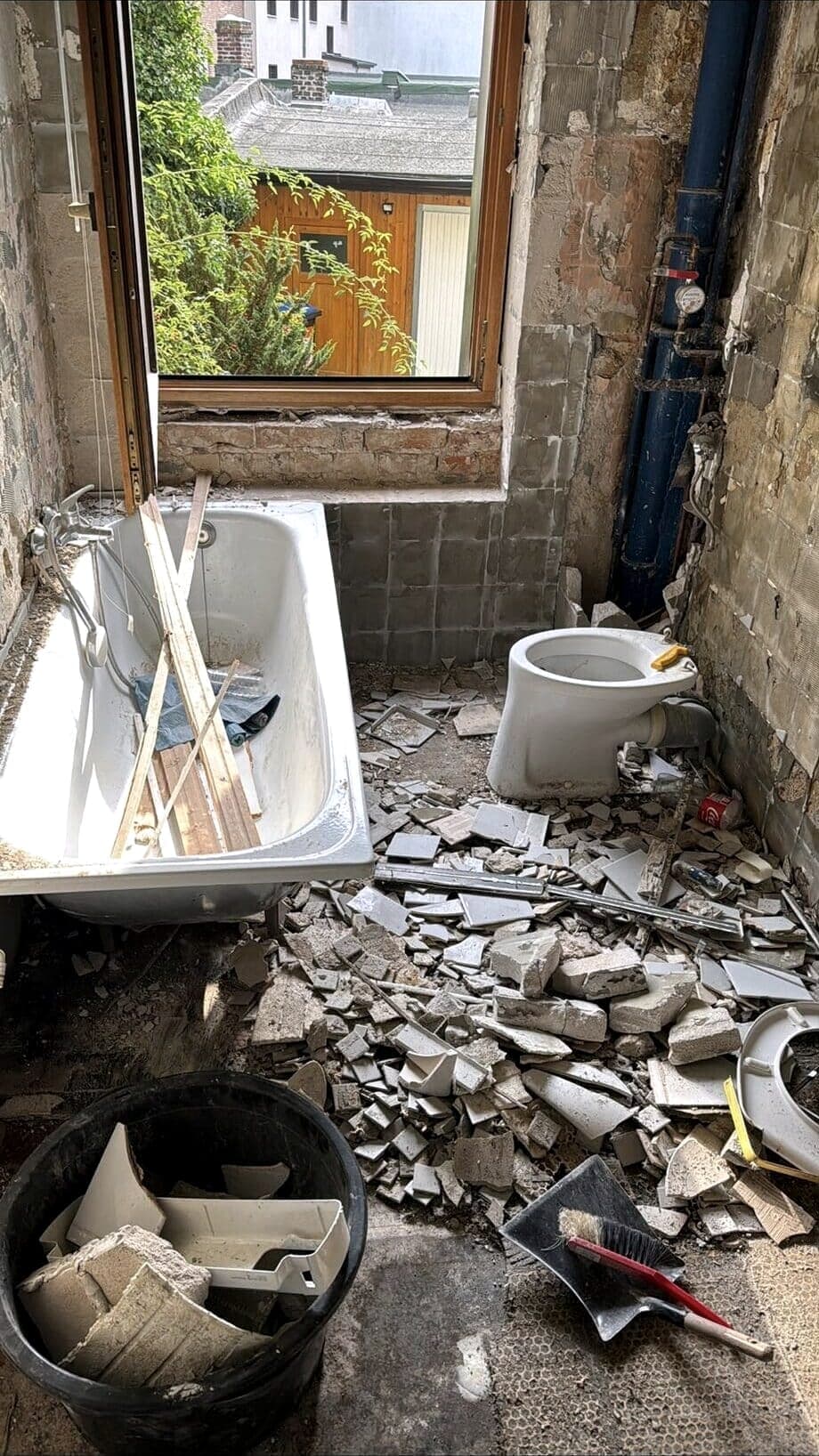 Bad im Altbau während des Rückbaus: abgeschlagene Fliesen, alte Wanne voller Schutt